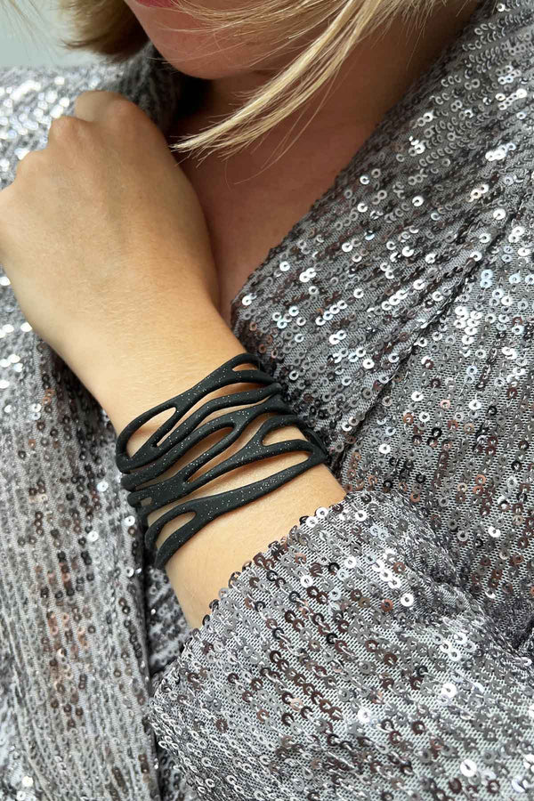 vue taille réelle, portée par mannequin, bracelet safari, couleur noir paillettes. Ladygum, marque française, bijoux fantaisies en silicone. Bracelet ajustable, réglable, souple, léger, minimisant les allergies. Le petit plus chic : la couleur noir avec paillettes. Style tribal, manchette, nature, ajouré, multirang, ethnique, tribal. Idée cadeau original.