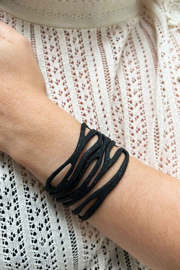 vue taille réelle, portée par mannequin, bracelet safari, couleur noir paillettes. Ladygum, marque française, bijoux fantaisies en silicone. Bracelet ajustable, réglable, souple, léger, minimisant les allergies. Le petit plus chic : la couleur noir avec paillettes. Style tribal, manchette, nature, ajouré, multirang, ethnique, tribal. Idée cadeau original.