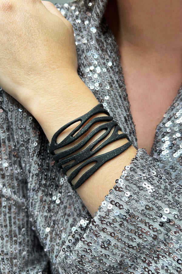 vue taille réelle, portée par mannequin, bracelet safari, couleur noir paillettes. Ladygum, marque française, bijoux fantaisies en silicone. Bracelet ajustable, réglable, souple, léger, minimisant les allergies. Le petit plus chic : la couleur noir avec paillettes. Style tribal, manchette, nature, ajouré, multirang, ethnique, tribal. Idée cadeau original.