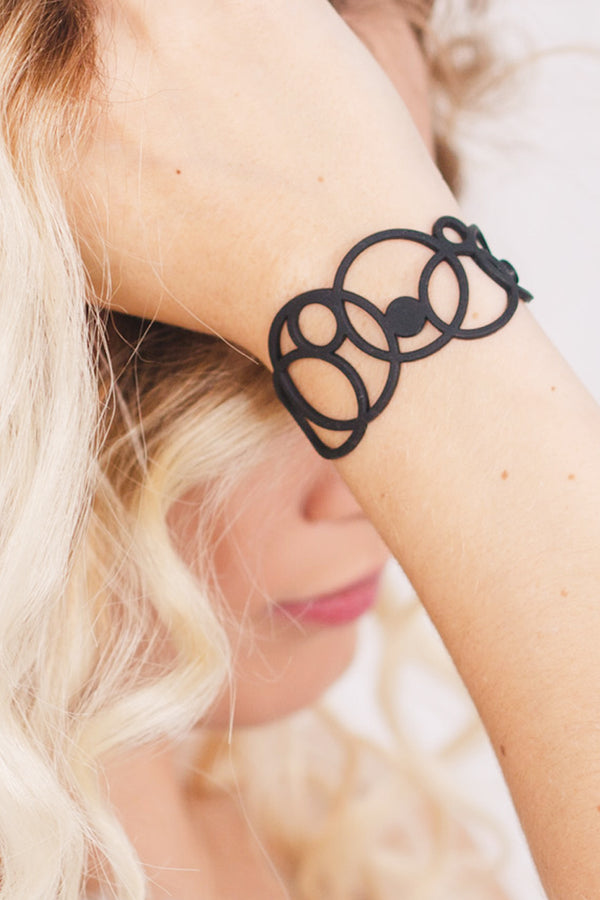 zoom, vue gros plan, bracelet disco, couleur noir. Vue taille réelle, porté sur poignet par mannequin Dorine Gaudin. Bijoux fantaisies en silicone, ladygum, marque française, créateurs, designers. Style manchette femme, rond, cercle, bulle, année 80, géométrique, contemporain. Léger, souple, longueur réglable, bracelet ajustable, fermoir en T, résistant à l'eau, à la chaleur, à la lumière, minimisant les allergies. Cadeau original.