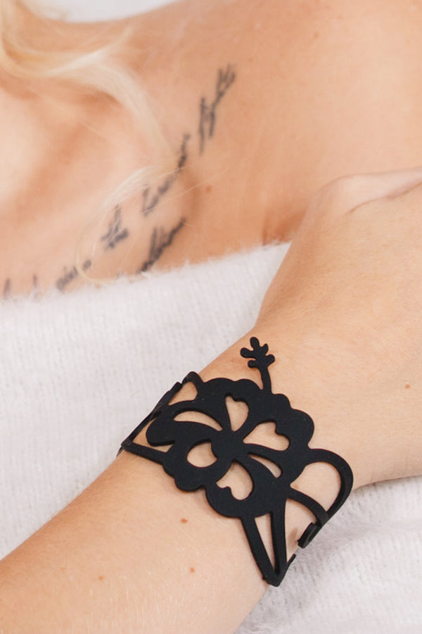 zoom, vue gros plan, bracelet hibiscus, couleur noir. Vue taille réelle, porté sur poignet par mannequin Dorine Gaudin. Bijoux fantaisies en silicone, ladygum, marque française, créateurs, designers. Style manchette femme, nature, fleur, floral, exotique, tropical, île, feuilles, plage. Léger, souple, longueur réglable, bracelet ajustable, fermoir en T, résistant à l'eau, à la chaleur, à la lumière, minimisant les allergies. Cadeau original.