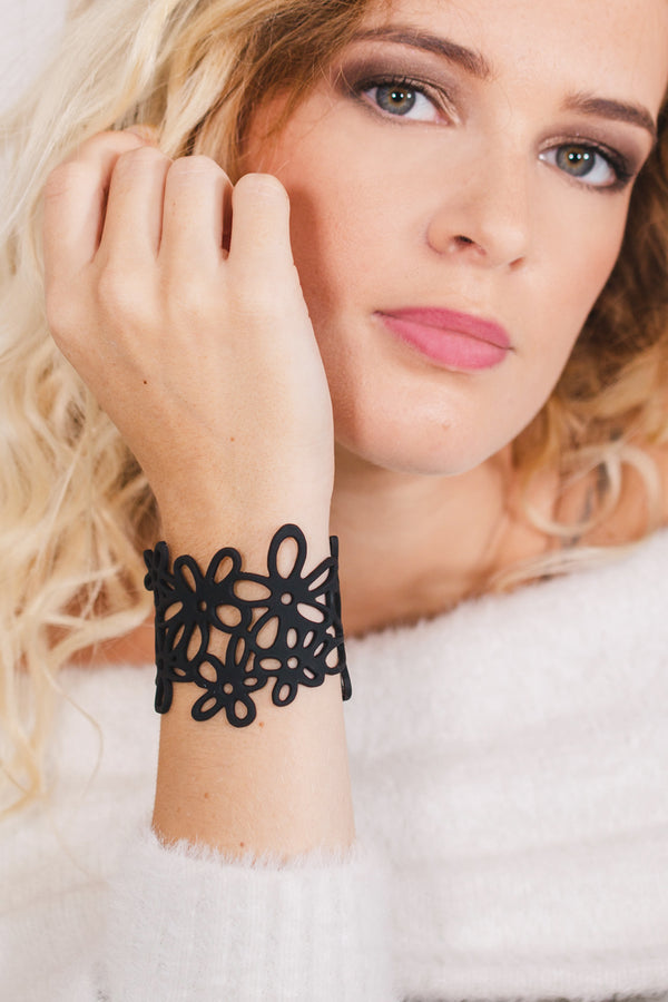 zoom, vue gros plan, bracelet hippie, couleur noir. Vue taille réelle, porté sur poignet par mannequin Dorine Gaudin. Bijoux fantaisies en silicone, ladygum, marque française, créateurs, designers. Style manchette femme, nature, fleur, floral, paquerette, marguerite, année 70. Léger, souple, longueur réglable, bracelet ajustable, fermoir en T, résistant à l'eau, à la chaleur, à la lumière, minimisant les allergies. Cadeau original.