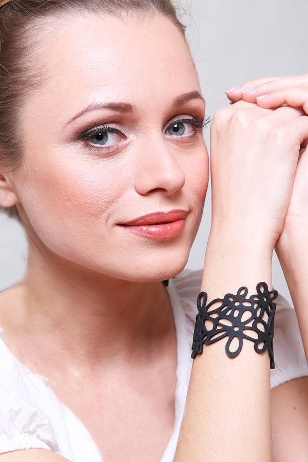 vue gros plan, taille réelle, porté par mannequin sur poignet, alla, bracelet hippie, couleur noir. Silicone, bijoux fantaisies, ladygum, marque française, créateurs, designers. Style manchette, fleur, nature, été, champêtre, plage, marguerite, paquerette, bohème, année 70. Souple, léger, résistant à l'eau, à la chaleur, à la lumière. Longueur réglable, bracelet ajustable. Fermoir en T, plusieurs trou pour régler à la bonne taille.