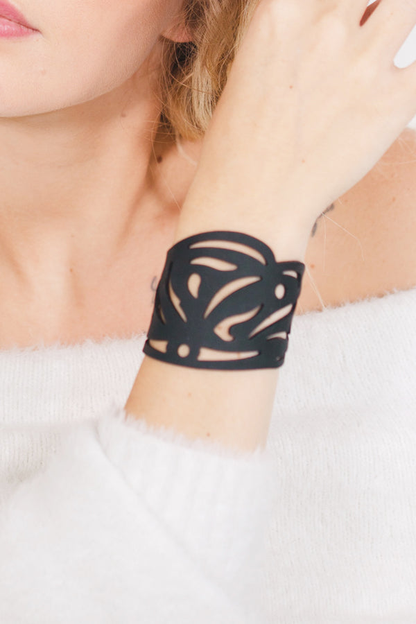 zoom, vue gros plan, bracelet maori, couleur noir. Vue taille réelle, porté sur poignet par mannequin Dorine Gaudin. Bijoux fantaisies en silicone, ladygum, marque française, créateurs, designers. Style nature, manchette femme, jungle, feuille, ajouré, tribal, ethnique, tatoo. Léger, souple, longueur réglable, bracelet ajustable, fermoir en T, résistant à l'eau, à la chaleur, à la lumière, minimisant les allergies. Cadeau original.