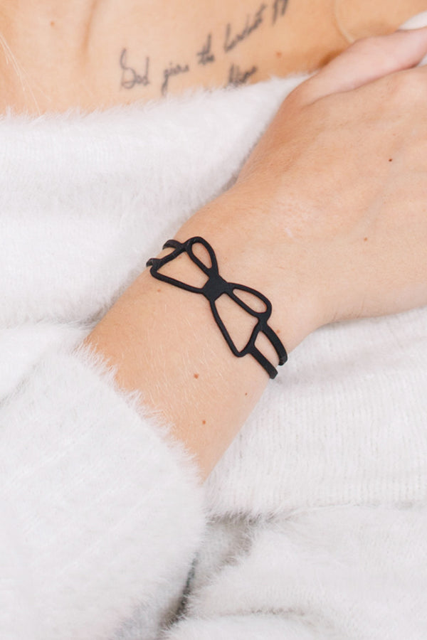 zoom, vue gros plan, bracelet noeud, couleur noir. Vue taille réelle, porté sur poignet par mannequin Dorine Gaudin. Bijoux fantaisies en silicone, ladygum, marque française, créateurs, designers. Style simple, minimaliste, noeud papillon, ruban, manchette femme. Léger, souple, longueur réglable, bracelet ajustable, fermoir en T, résistant à l'eau, à la chaleur, à la lumière, minimisant les allergies. Cadeau original.