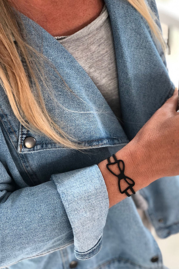 vue bracelet noeud, noir, silicone, gros plan, taille réelle, porté par la créatrice Morgane. Bijoux fantaisies, ladygum, marque française, créateurs, designers. Style minimaliste, féminin, noeud papillon, ruban, fille, couture. Léger, souple, longueur réglable, bracelet ajustable, fermoir en T.