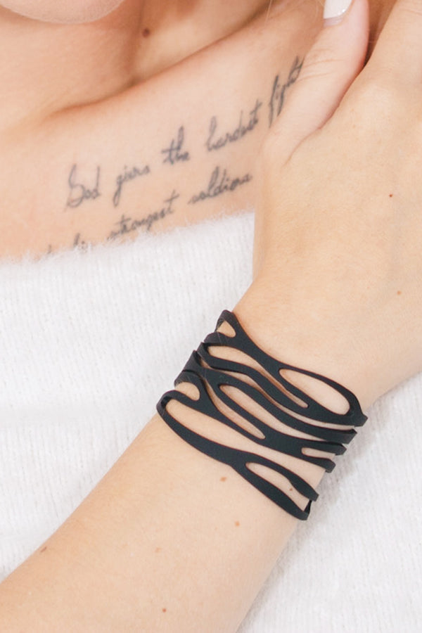 zoom, vue gros plan, bracelet safari, couleur noir. Vue taille réelle, porté sur poignet par mannequin Dorine Gaudin. Bijoux fantaisies en silicone, ladygum, marque française, créateurs, designers. Style manchette femme, ajouré, tribal, tatoo, ethnique, courbes, abstrait. Léger, souple, longueur réglable, bracelet ajustable, fermoir en T, résistant à l'eau, à la chaleur, à la lumière, minimisant les allergies. Cadeau original.