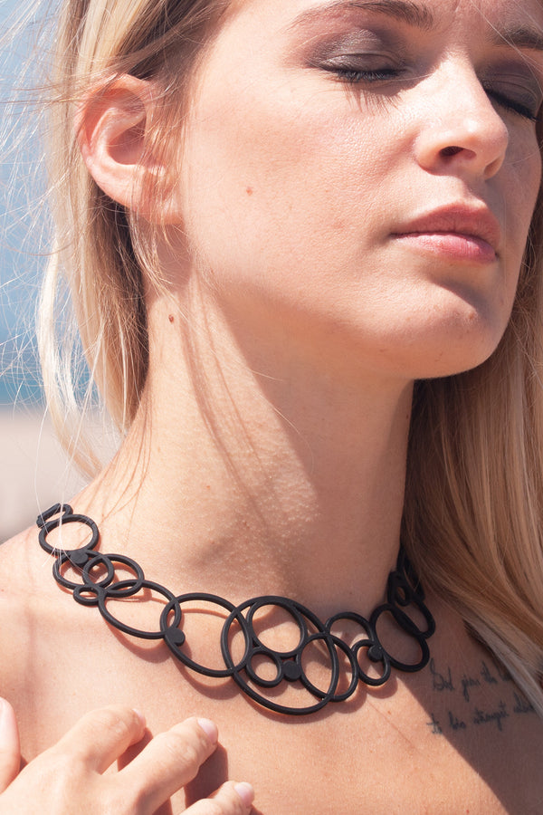 zoom, vue gros plan, collier disco, couleur noir, dispo en rouge. Taille réelle. Bijoux fantaisies en silicone, ladygum, marque française, créateurs, designers. Style plastron, large, grand, graphique, géométrique, contemporain, rond, cercle, bulle, année 80. Léger, souple, longueur réglable, ajustable, minimisant les allergies, résistant à l'eau, à la chaleur, fermoir en T. Cadeau original.