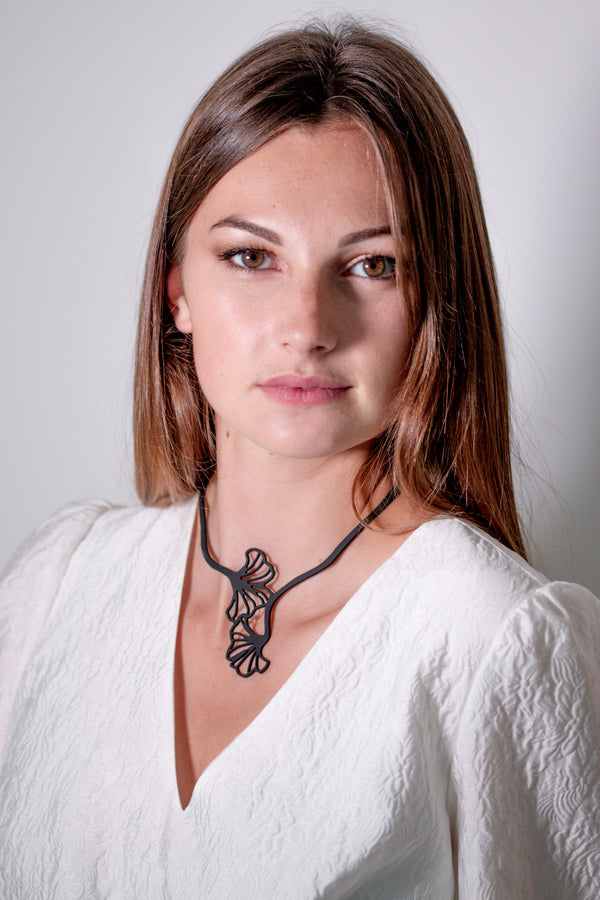vue taille réelle, collier ginkgo, porté par mannequin, youna. Silicone, noir, bijoux fantaisies, ladygum, marque française, créateurs, designers. Souple, léger, minimisant les allergies, résistant à l'eau, à la chaleur, longueur réglable, bijoux ajustables. Style feuilles, printemps, japon, nature, fleurs, floral, fleuri. Modèle ginkgo.