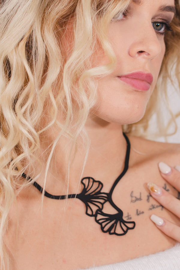 vue taille réelle, collier ginkgo, porté par mannequin, dorine gaudin. Silicone, noir, bijoux fantaisies, ladygum, marque française, créateurs, designers. Souple, léger, minimisant les allergies, résistant à l'eau, à la chaleur, longueur réglable, bijoux ajustables. Style feuilles, printemps, japon, nature, fleurs, floral, fleuri. Modèle ginkgo.