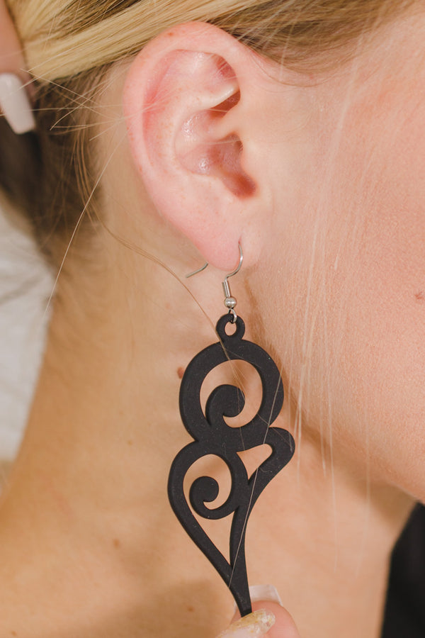 zoom, vue gros plan, paire de boucles d'oreilles courbe, grand modèle, couleur noir. Portées par mannequin Dorine Gaudin. Bijoux fantaisies en silicone, marque française, créateurs, designers. Style fleur, floral, rond, longues, pendantes. Attache dormeuse en acier inoxydable. Minimisant les allergies, résistant à l'eau/à la chaleur/à la lumière, souple, léger. Cadeau original.