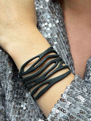 vue taille réelle, portée par mannequin, bracelet safari, couleur noir paillettes. Ladygum, marque française, bijoux fantaisies en silicone. Bracelet ajustable, réglable, souple, léger, minimisant les allergies. Le petit plus chic : la couleur noir avec paillettes. Style tribal, manchette, nature, ajouré, multirang, ethnique, tribal. Idée cadeau original.