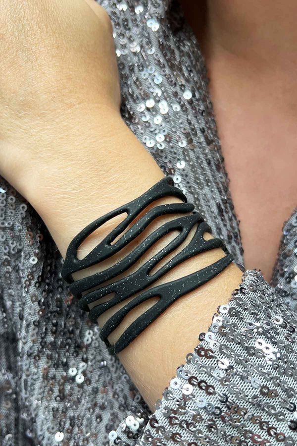 vue taille réelle, portée par mannequin, bracelet safari, couleur noir paillettes. Ladygum, marque française, bijoux fantaisies en silicone. Bracelet ajustable, réglable, souple, léger, minimisant les allergies. Le petit plus chic : la couleur noir avec paillettes. Style tribal, manchette, nature, ajouré, multirang, ethnique, tribal. Idée cadeau original.