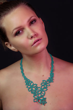 zoom, vue gros plan, collier fleur de tiaré, modèle long, couleur turquoise. Vue taille réelle, porté par mannequin dorine gaudin. Bijoux fantaisies en silicone, ladygum, marque française, créateurs, designers. Style long, pendant, plongeant, fleur, feuilles, nature, floral, jasmin, été, pétales. Léger, souple, résistant à l'eau/à la chaleur/à la lumière. Collier ajustable, longueur réglable, fermoir en T. Cadeau original.