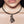 zoom, vue gros plan, collier pendentif rose japonaise long, couleur noir. Vue taille réelle, porté. Silicone, ladygum, bijoux fantaisies, marque française, créateurs, designers. Style simple, minimaliste. Collier simplissimo avec strass couleur cristal, amovible, riveté, avec pendentif boucle rose japonaise long, nature, fleur, amour, romantique. Léger, souple, résistant à l'eau, à la chaleur, à la lumière. Collier ajustable, longueur réglable, fermoir en T. Cadeau original. 