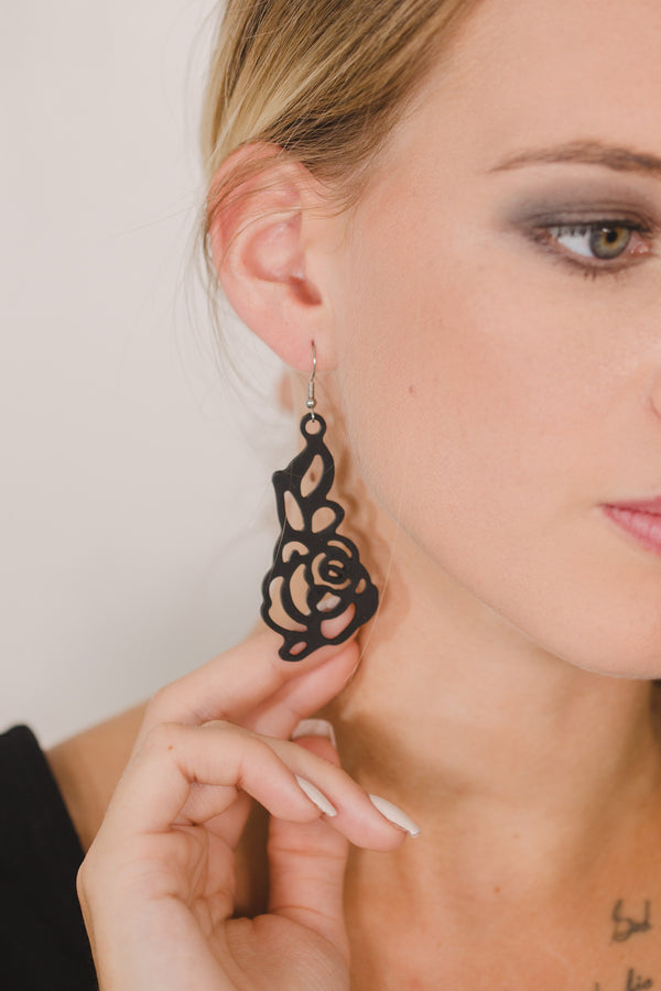 zoom, gros plan, vue boucles d'oreilles rose japonaise modèle long, couleur noir. Portées par mannequin dorine gaudin. Attache dormeuse en acier inoxydable. Silicone, marque française, ladygum, bijoux fantaisies en silicone. Style fleur, floral, nature, romantique, pendantes, longues. Résistante à l'eau/à la chaleur/à la lumière. Souple, léger, original.