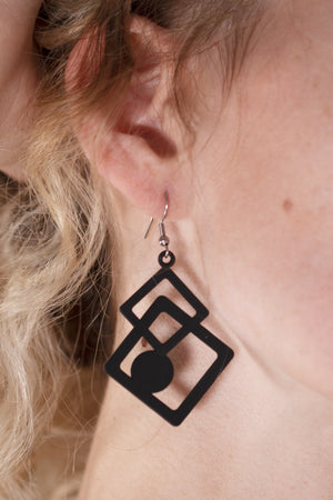 vue en entier, sur mannequin, taille réelle, paire de boucles d'oreilles, modèle Tétris, couleur noir. Ladygum, marque française, bijoux fantaisies en silicone, créateurs, designers. Style carré, graphique, puzzle, cube, contemporain. Attache dormeuse en acier inoxydable, souples légères. Cadeau original.