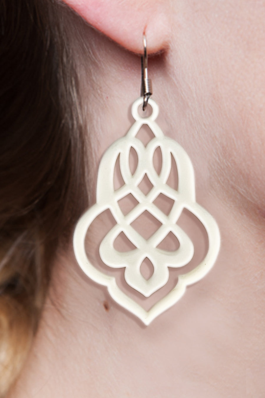 vue gros plan, zoom, paire de boucles d'oreilles arabesque, couleur blanc. Vue portée sur mannequin. LadyGum, bijoux fantaisies en silicone, créateurs, designers. Style celtique, baroque, gothique, tribal, pendante. Attache dormeuse en acier inoxydable, légères, souples, waterproof. Cadeau original.