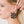 zoom, vue gros plan, paire de boucles d'oreilles hibiscus, couleur noir. Portées par mannequin Dorine Gaudin. Bijoux fantaisies en silicone, marque française, créateurs, designers. Style tropical, fleur, floral, nature, île, exotique, jungle, plage, mer. Attache dormeuse en acier inoxydable. Minimisant les allergies, résistant à l'eau/à la chaleur/à la lumière, souple, léger. Cadeau original.
