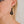 zoom, vue gros plan, paire de boucles d'oreilles clochette, couleur noir. Portées par mannequin Dorine Gaudin. Bijoux fantaisies en silicone, marque française, créateurs, designers. Style nature, fleur, floral, pendante, courte, feuille. Attache dormeuse en acier inoxydable. Minimisant les allergies, résistant à l'eau/à la chaleur/à la lumière, souple, léger. Cadeau original.
