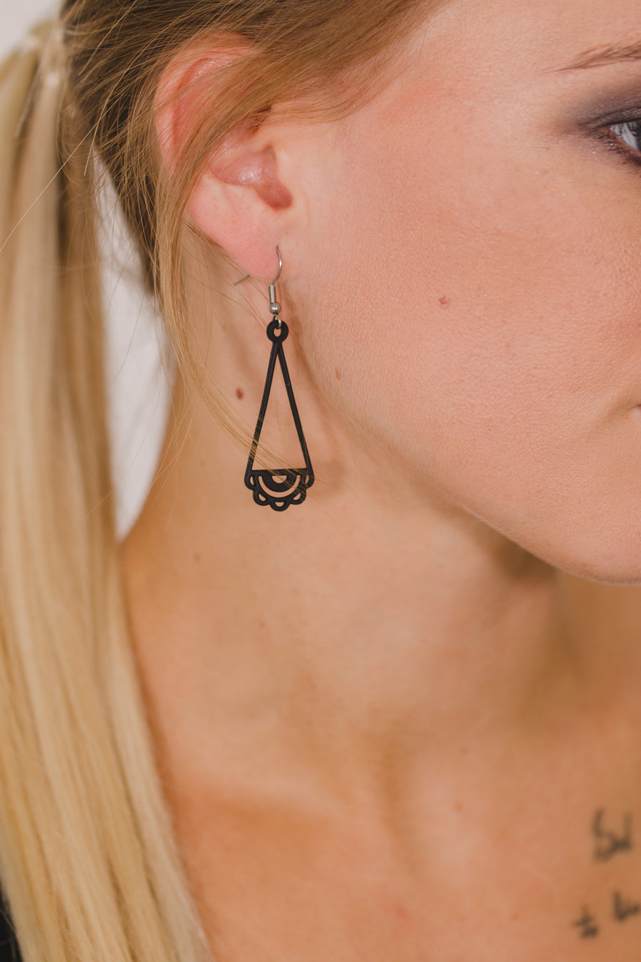 zoom, vue gros plan, paire de boucles d'oreilles dentelle, couleur noir. Portées par mannequin Dorine Gaudin. Bijoux fantaisies en silicone, marque française, créateurs, designers. Style pendante, géométrique, graphique, féminin, minimaliste, motif. Attache dormeuse en acier inoxydable. Minimisant les allergies, résistant à l'eau/à la chaleur/à la lumière, souple, léger. Cadeau original.