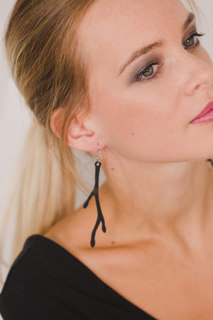 zoom, vue gros plan, paire de boucles d'oreilles primavera, couleur noir. Portées par mannequin Dorine Gaudin. Bijoux fantaisies en silicone, marque française, créateurs, designers. Style longue, pendante, fleur, nature. Attache dormeuse en acier inoxydable. Minimisant les allergies, résistant à l'eau/à la chaleur/à la lumière, souple, léger. Cadeau original.