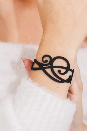 zoom, vue gros plan, bracelet courbe, couleur noir. Vue taille réelle, porté sur poignet par mannequin Dorine Gaudin. Bijoux fantaisies en silicone, ladygum, marque française, créateurs, designers. Style nature, manchette femme, fleur, rond, cercle, tourbillon, abstrait, contemporain. Léger, souple, longueur réglable, bracelet ajustable, fermoir en T, résistant à l'eau, à la chaleur, à la lumière, minimisant les allergies. Cadeau original.