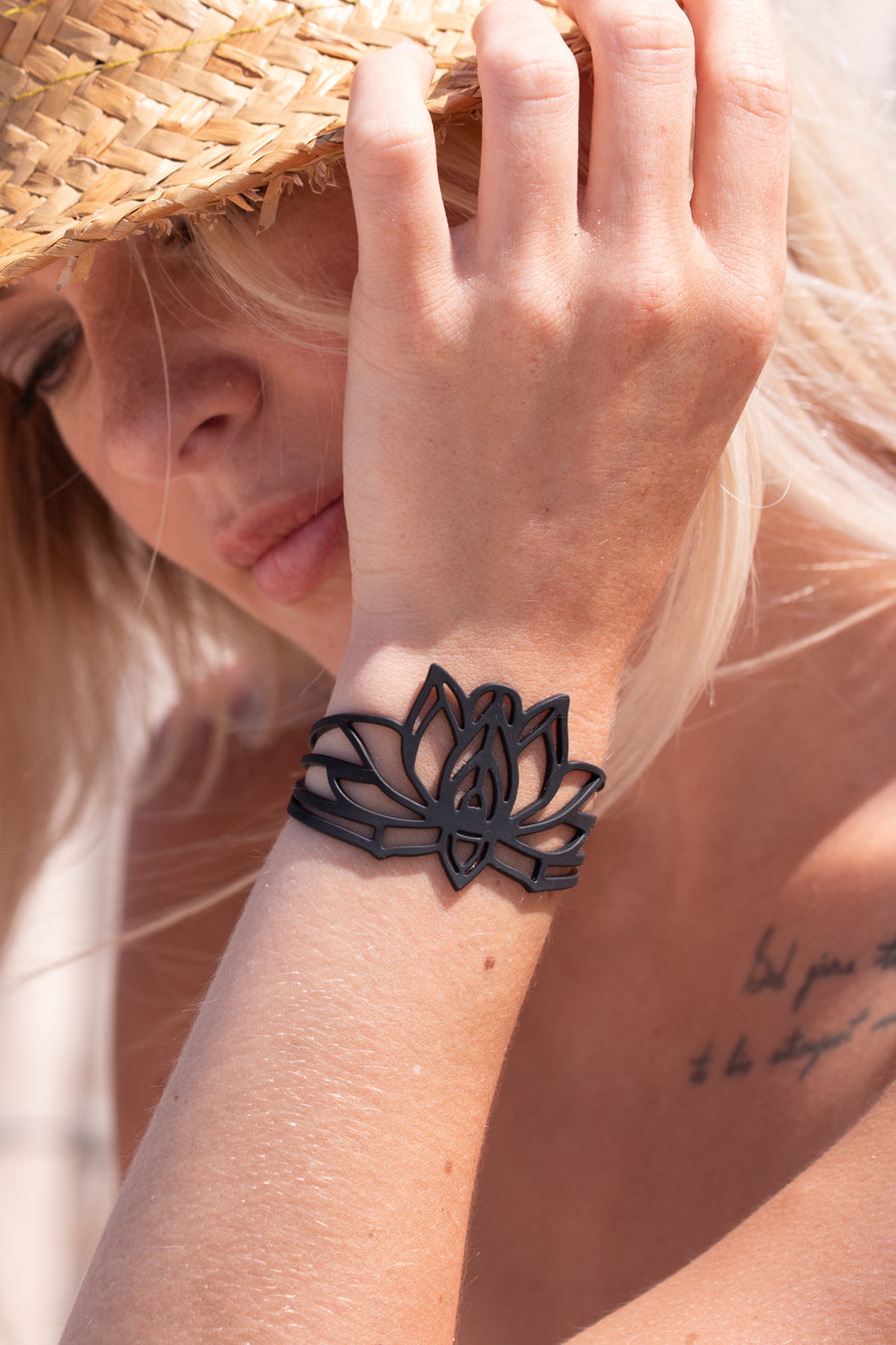 zoom, vue gros plan, bracelet mantra, couleur noir. Vue taille réelle, porté sur poignet par mannequin Dorine Gaudin. Bijoux fantaisies en silicone, ladygum, marque française, créateurs, designers. Style nature, manchette femme, fleur, floral, zen, lotus, nénuphar, yoga, feuille, plante. Léger, souple, longueur réglable, bracelet ajustable, fermoir en T, résistant à l'eau, à la chaleur, à la lumière, minimisant les allergies. Cadeau original.