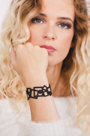 zoom, vue gros plan, bracelet tétris, couleur noir. Vue taille réelle, porté sur poignet par mannequin Dorine Gaudin. Bijoux fantaisies en silicone, ladygum, marque française, créateurs, designers. Style manchette femme, carré, cube, géométrique, contemporain. Léger, souple, longueur réglable, bracelet ajustable, fermoir en T, résistant à l'eau, à la chaleur, à la lumière, minimisant les allergies. Cadeau original.
