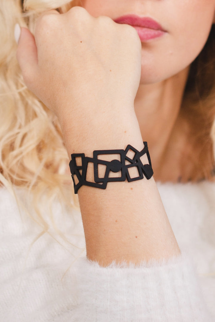 zoom, vue gros plan, bracelet tétris, couleur noir. Vue taille réelle, porté sur poignet par mannequin Dorine Gaudin. Bijoux fantaisies en silicone, ladygum, marque française, créateurs, designers. Style manchette femme, carré, cube, géométrique, contemporain. Léger, souple, longueur réglable, bracelet ajustable, fermoir en T, résistant à l'eau, à la chaleur, à la lumière, minimisant les allergies. Cadeau original.