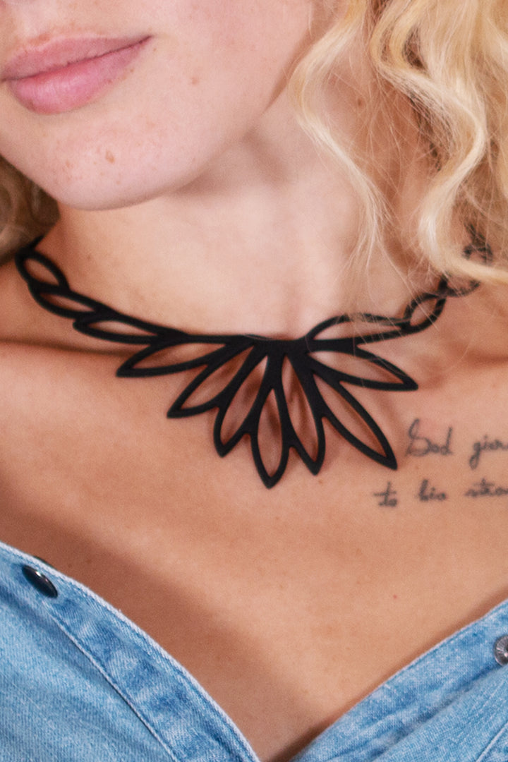 vue gros plan, taille réelle, collier lotus porté sur mannequin, dorine gaudin. Silicone, noir, ladygum, marque française, bijoux fantaisies, créateurs, designers. Style fleur, floral, feuille, zen, minimaliste. Léger, souple, longueur réglable, ajustable, minimisant les allergies, résistant à l'eau, à la chaleur. Modèle lotus.