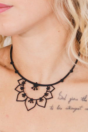 zoom, vue gros plan, collier nymphéa, couleur noir. Vue taille réelle, porté par mannequin dorine gaudin. Bijoux fantaisies en silicone, ladygum, marque française, créateurs, designers. Style fleur, nature, floral, pampilles, zen, yogo, lotus, nénuphar, pétales. Léger, souple, résistant à l'eau/à la chaleur/à la lumière. Collier ajustable, longueur réglable, fermoir en T. Cadeau original.
