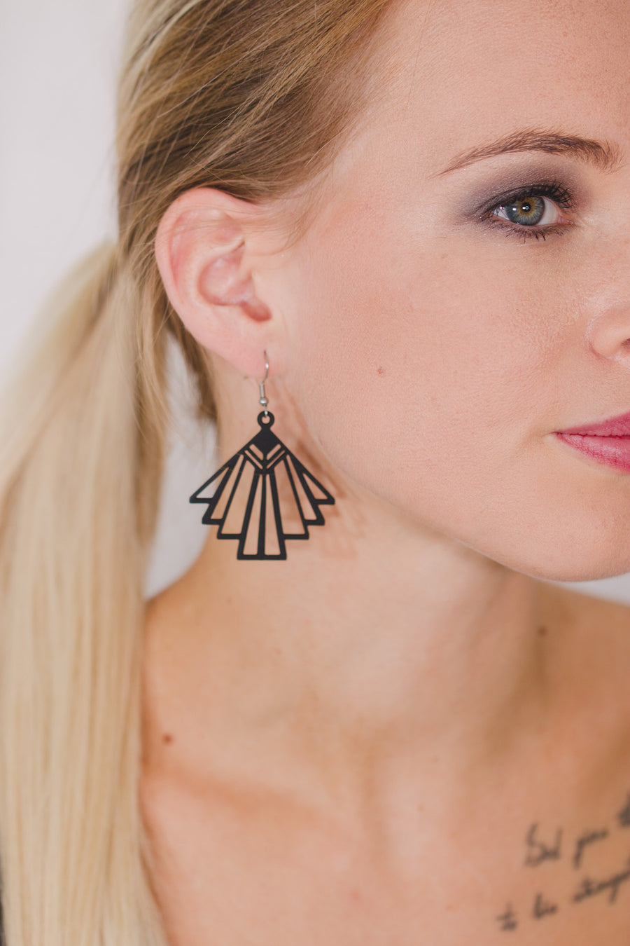 zoom, vue gros plan, paire de boucles d'oreilles charleston, couleur noir. Portées par mannequin Dorine Gaudin. Bijoux fantaisies en silicone, marque française, créateurs, designers. Style éventail, art déco, rétro, géométrique, graphique, moderne, contemporain. Attache dormeuse en acier inoxydable. Minimisant les allergies, résistant à l'eau/à la chaleur/à la lumière, souple, léger. Cadeau original.