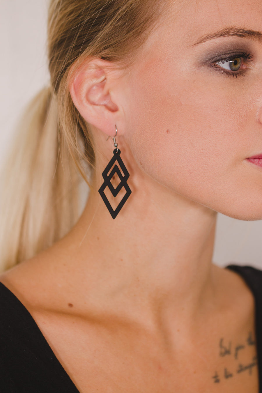 zoom, vue gros plan, paire de boucles d'oreilles diamant, couleur noir. Portées par mannequin Dorine Guadin. Bijoux fantaisies en silicone, marque française, créateurs, designers. Style losange, triangle, géométrique, graphique, moderne, contemporain. Attache dormeuse en acier inoxydable. Minimisant les allergies, résistant à l'eau/à la chaleur/à la lumière, souple, léger. Cadeau original.