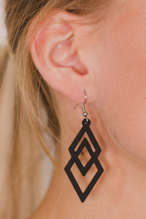 zoom, vue gros plan, paire de boucles d'oreilles diamant, couleur noir. Portées par mannequin Dorine Guadin. Bijoux fantaisies en silicone, marque française, créateurs, designers. Style losange, triangle, géométrique, graphique, moderne, contemporain. Attache dormeuse en acier inoxydable. Minimisant les allergies, résistant à l'eau/à la chaleur/à la lumière, souple, léger. Cadeau original.